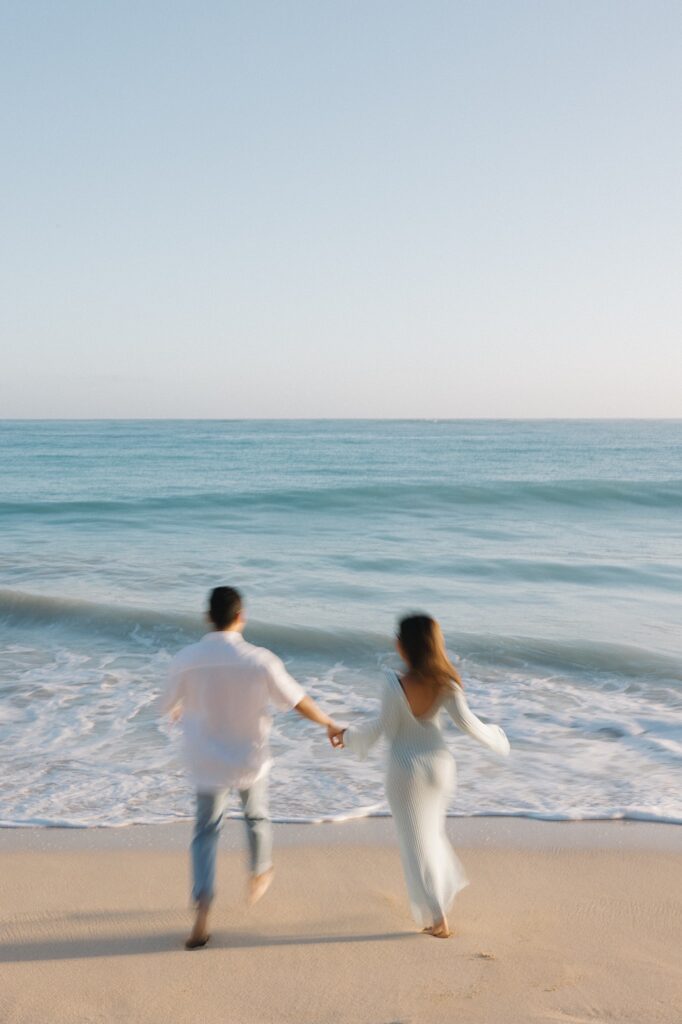 Out of focus photo of a man and woman holding hands while running towards the ocean at Waimanalo Beach