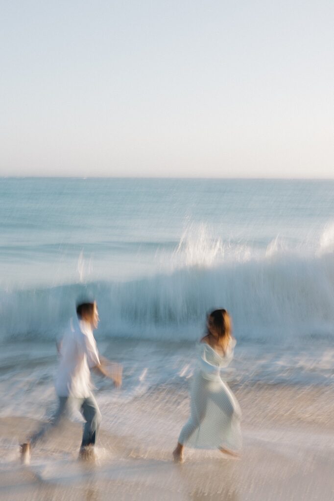 Out of focus photo of a man and woman running along Waimanalo Beach together as waves crash in the background