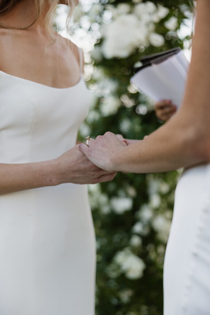 Close up photo of two brides holding hands during their wedding ceremony