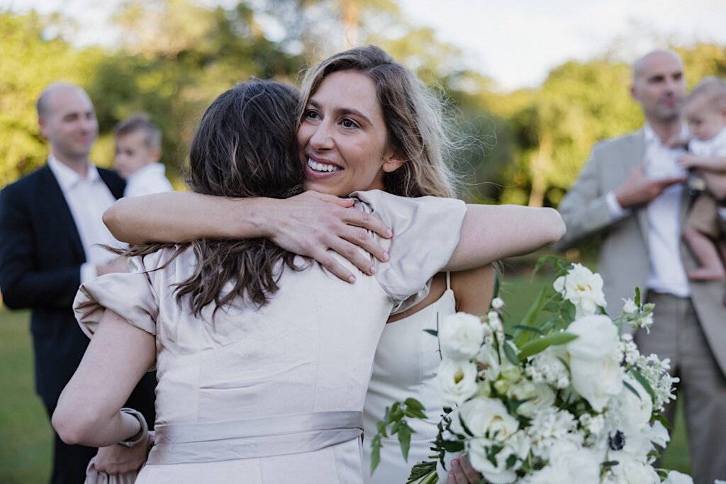 A bride smiles while hugging a guest of her outdoor LGBTQ wedding at Loulu Palm on Oahu