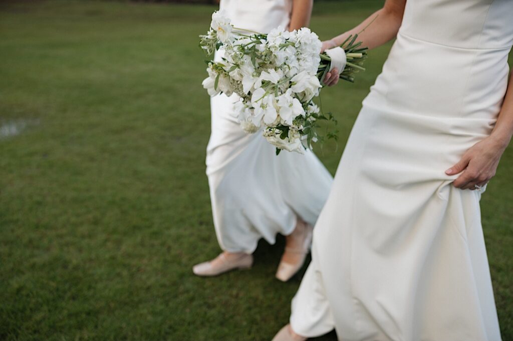 Close up photo of two brides walking side by side in the grass of Loulu Palm on Oahu after their LGBTQ wedding ceremony