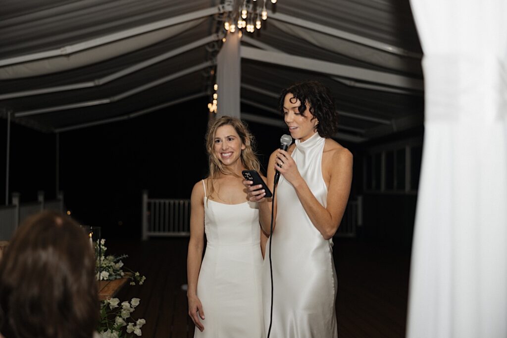 2 brides stand side by side as one gives a speech during the reception for their LGBTQ wedding at Loulu Palm on Oahu