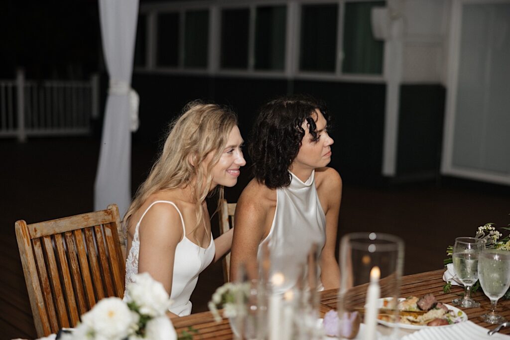 2 brides sit next to one another during their LGBTQ wedding reception at Loulu Palm on Oahu