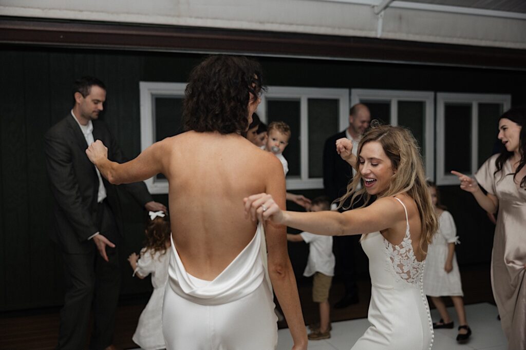 2 brides dance with one another along with the guests of their LGBTQ wedding during their outdoor reception at Loulu Palm on Oahu
