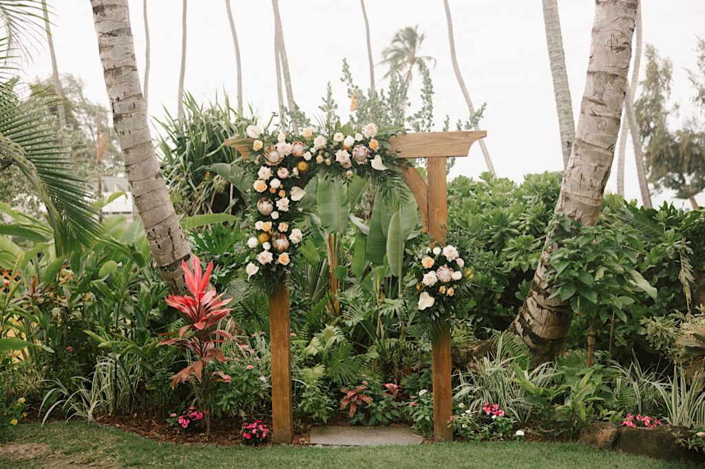 A wooden archway is decorated with pastel flowers at the wedding venue, Male'ana Gardens on Oahu