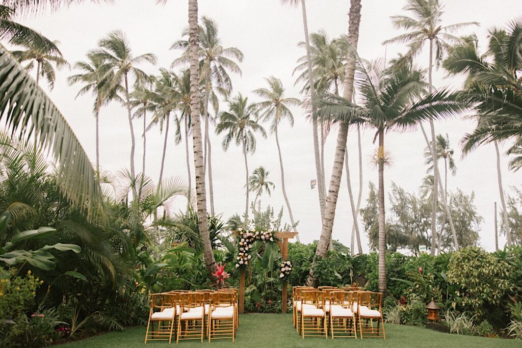 The ceremony space of the wedding venue, Male'ana Gardens on Oahu is set up with chairs and pastel flowers on the wooden archway