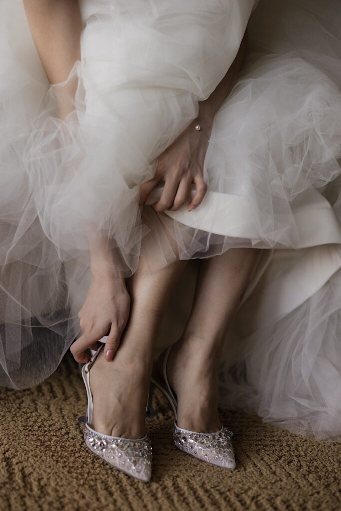 Close up photo of a bride in her wedding dress sitting down as she puts on her shoes