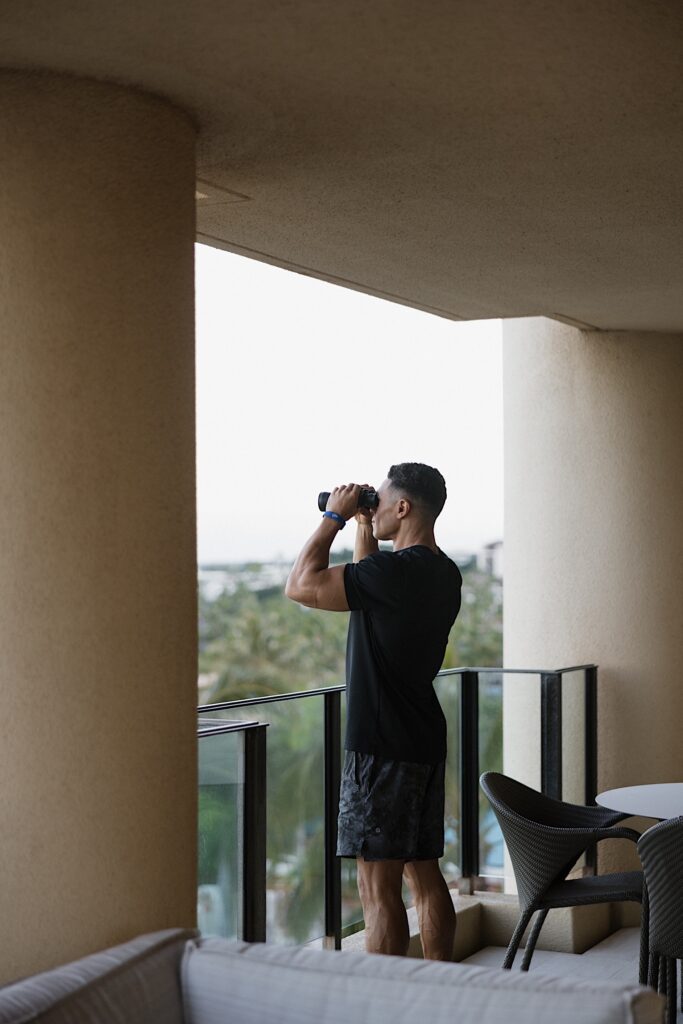 Jay looks out at the ocean with a pair of binoculars from the balcony of his room at the Four Seasons Resort on Maui