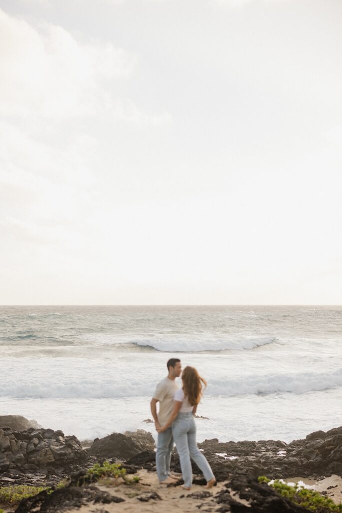 A couple hold hands and are about to kiss one another while standing on the shore of Makapuu Beach on Oahu
