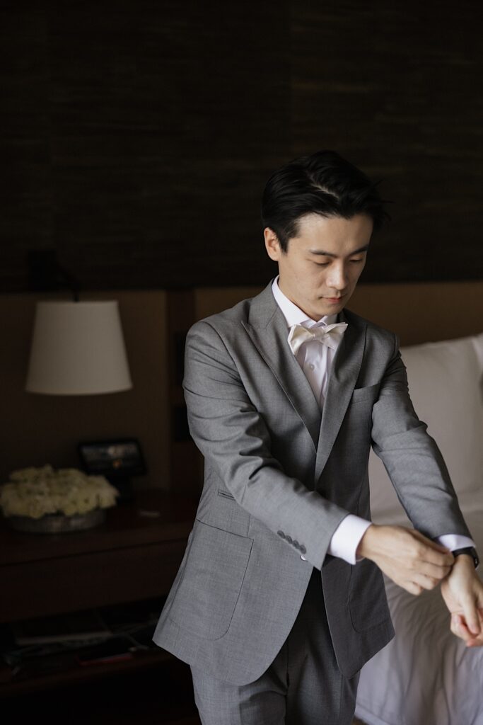 A groom stands in his hotel room at the Four Seasons Oahu in Ko Olina and adjusts the cuffs of his suit
