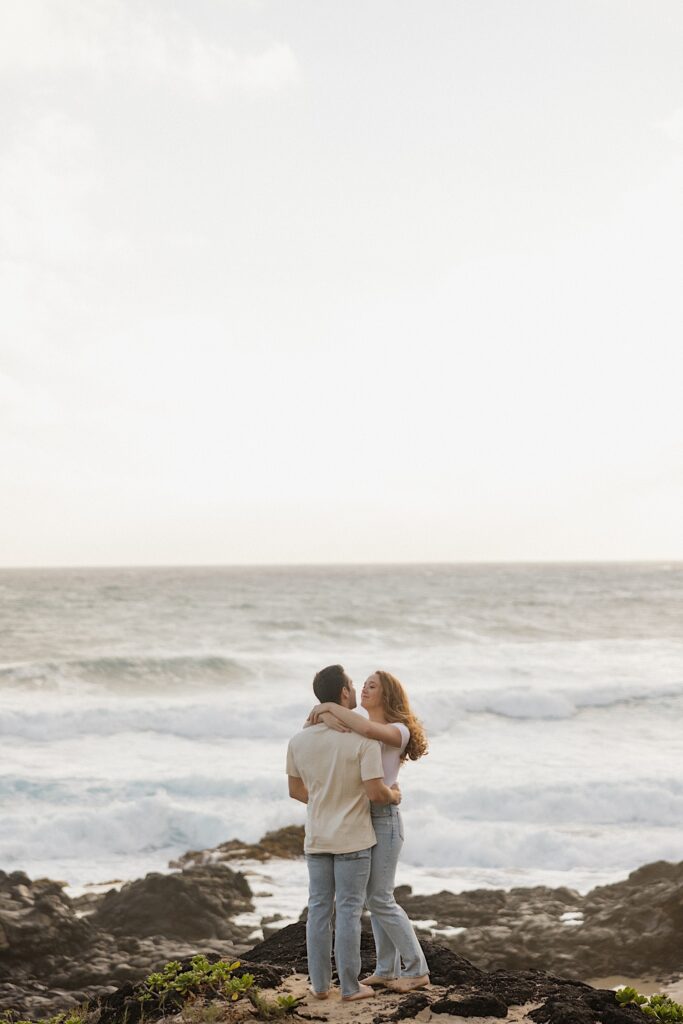 A woman wraps her arms around a man as he hugs her while they stand together on Makapuu Beach of Oahu