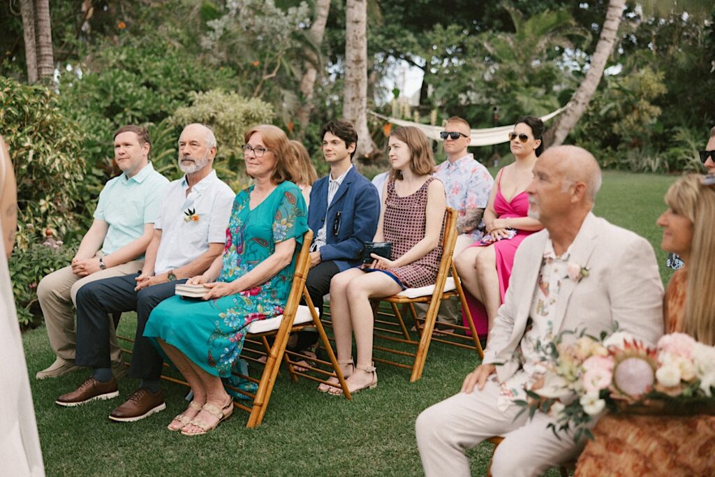 Guests of an intimate wedding at the venue Male'ana Gardens on Oahu sit and watch as the ceremony takes place