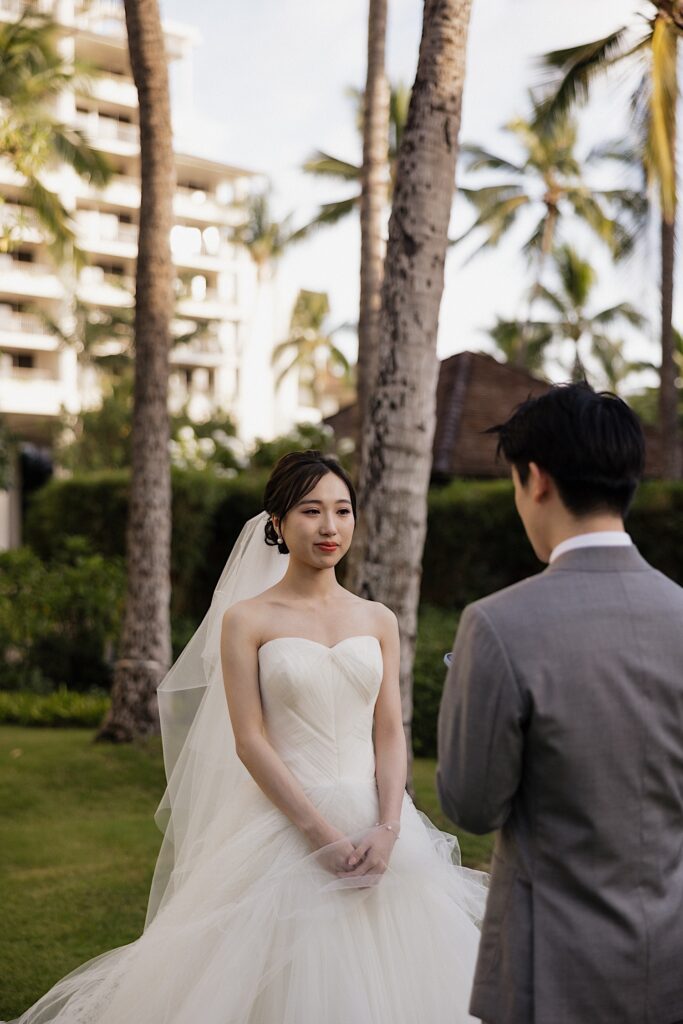 A bride stands and listens as the groom reads his private vows to her while the two stand under palm trees