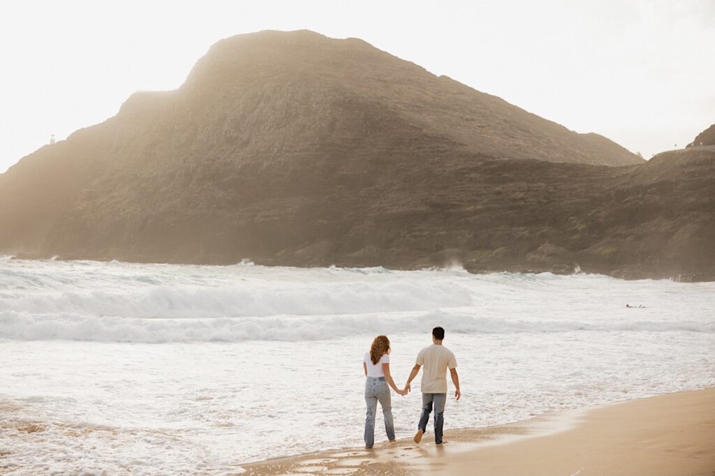 During their romantic honeymoon session a couple walk hand in hand away from the camera along the waterline of Makapuu Beach on Oahu, Hawaii