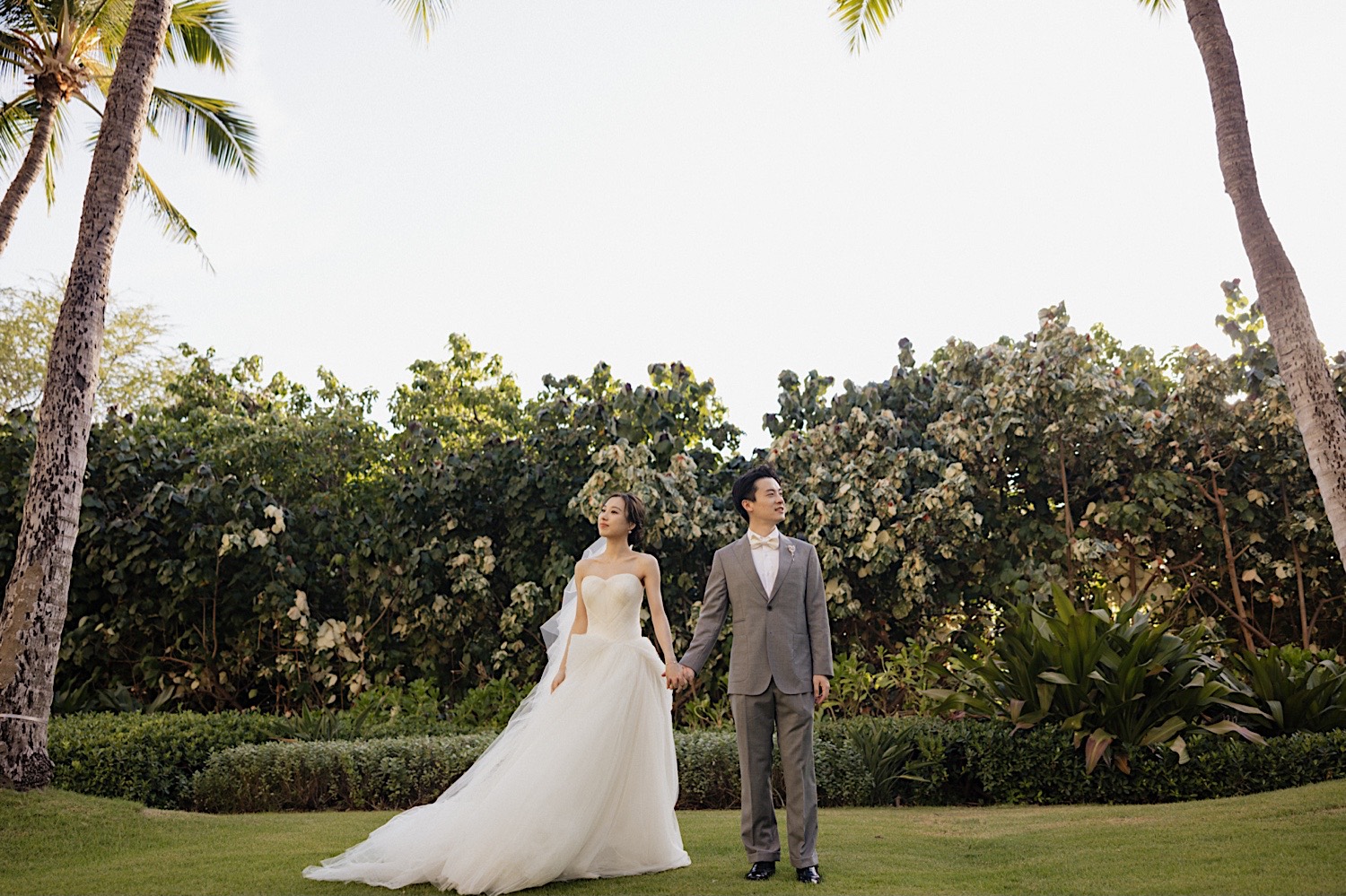At one of the ceremony spaces at the Four Seasons Oahu in Ko Olina, a bride and groom hold hands and look away from one another before their elopement ceremony
