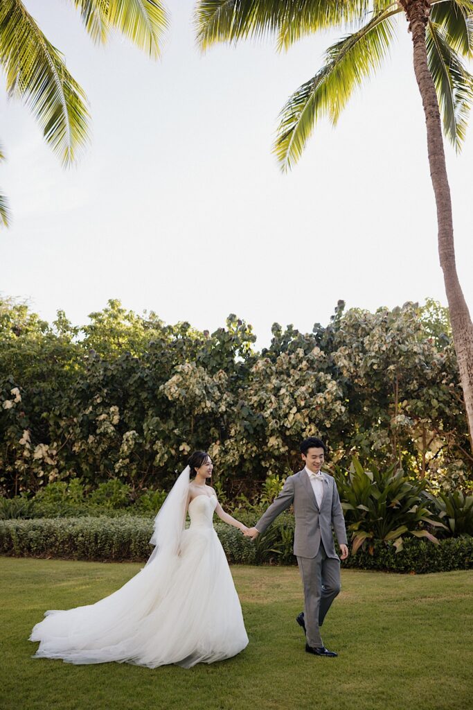 A bride and groom walk hand in hand along one of the outdoor ceremony spaces at the Four Seasons Oahu in Ko Olina