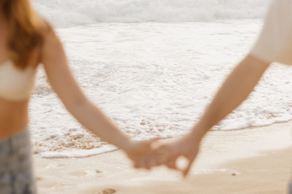 Close up photo of a couple holding hands while looking out at the waves of the ocean during their romantic honeymoon session at Makapuu Beach on Oahu, Hawaii