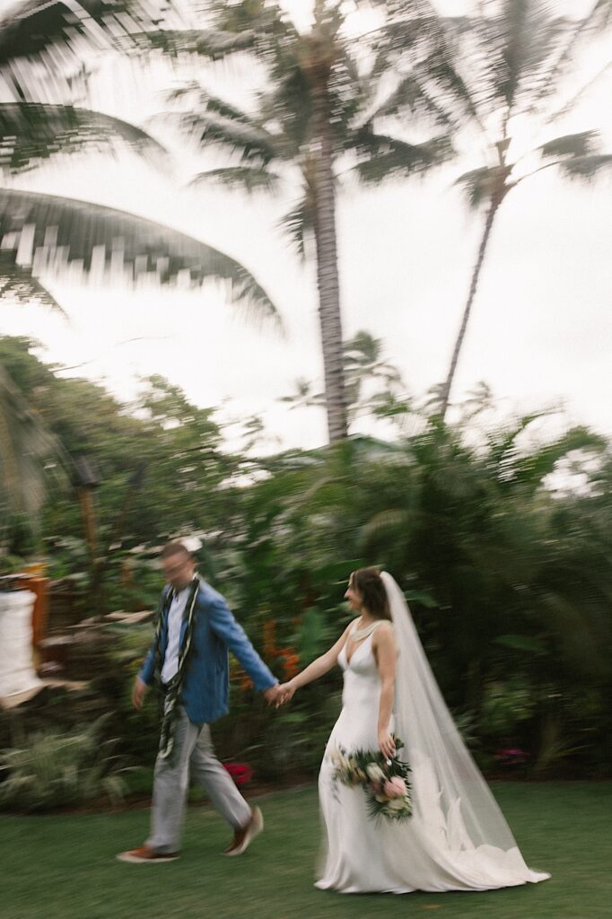 A bride and groom walk hand in hand on the grounds of Male'ana Gardens on Oahu after their ceremony