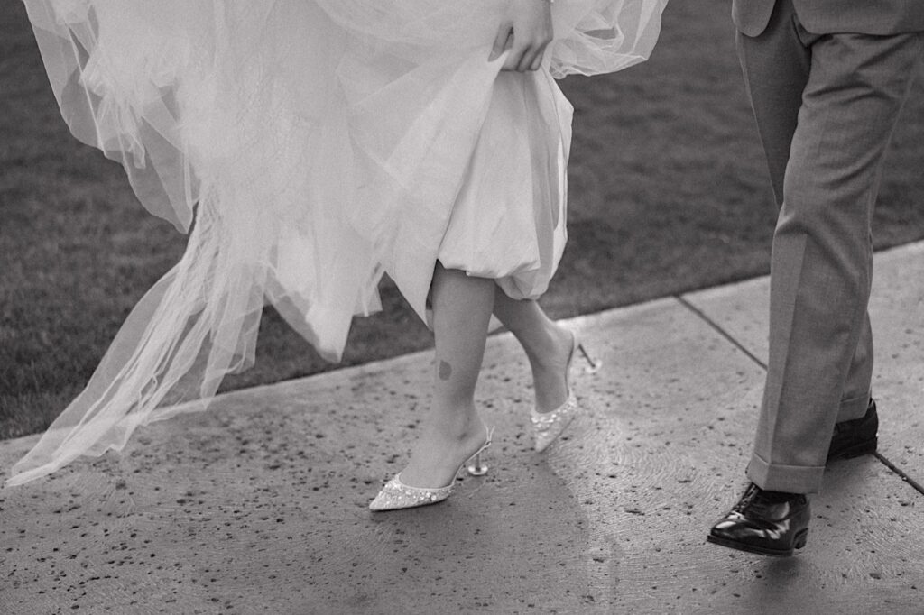 Black and white close up photo of a bride and groom's legs as they walk along a sidewalk at the Four Seasons Oahu in Ko Olina towards their elopement ceremony space