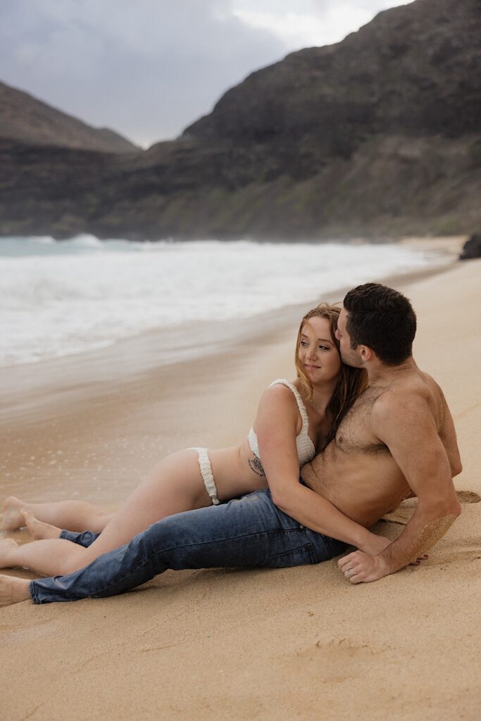 A woman lays on a man while he lays on Makapuu Beach of Oahu, the woman is looking back out at the ocean while the man kisses her head