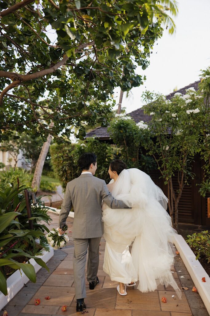A bride and groom walk side by side down a path lined with tropical plants at the Four Seasons Oahu in Ko Olina