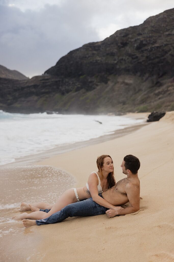 A woman lays on a man who is laying on his back on Makapuu Beach during their honeymoon session