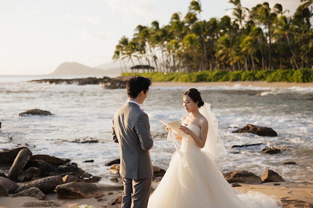 A bride reads her vows to the groom while they stand together on a beach near the Four Seasons Oahu in Ko Olina during their elopement ceremony