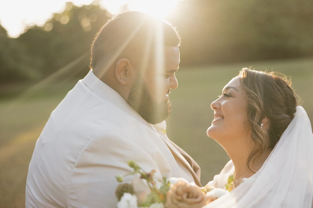A bride and groom smile at one another while the sun sets behind them during golden hour portraits