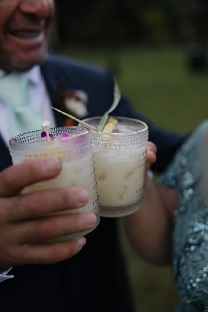 Close up photo of drinks being toasted together during cocktail hour by guests of a wedding