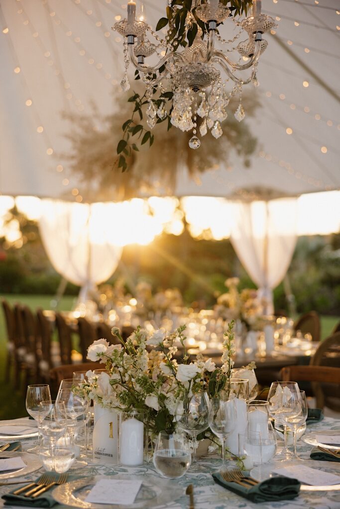A table decorated for a wedding reception sits under a tent while the sun sets in the background