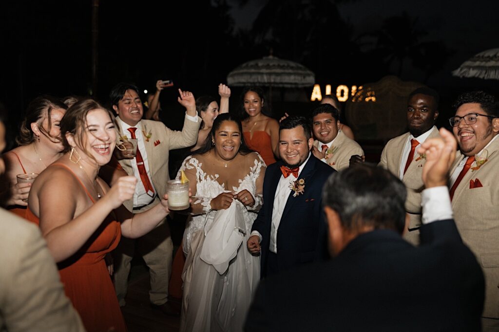 A bride and groom smile as they dance with guests of their wedding party during their reception at a villa on Oahu