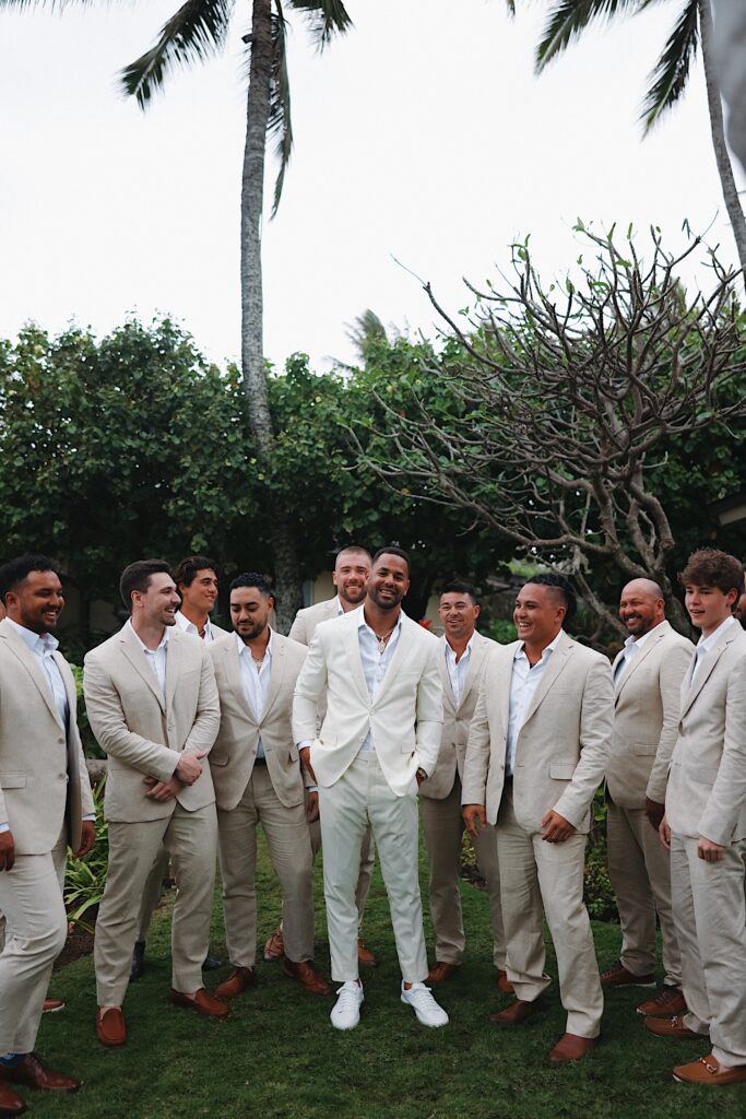 A groom stands with his 9 groomsmen around him on a lawn before his wedding ceremony