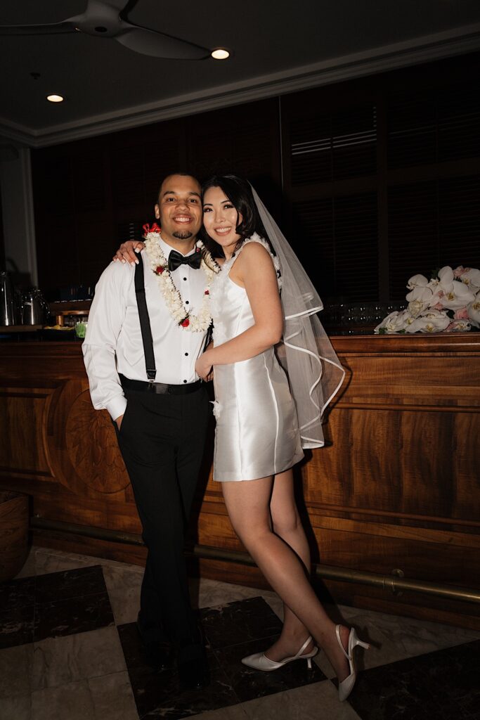 A bride and groom smile for a photo together while standing next to a bar