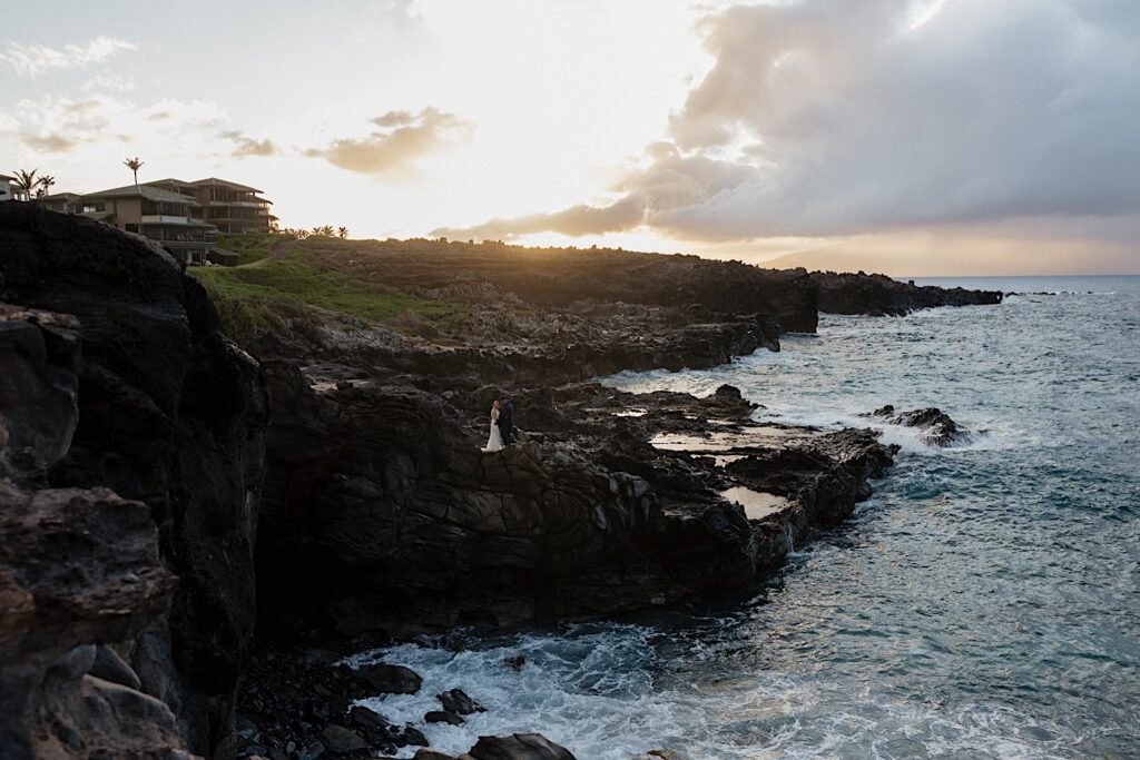 Bride and groom are captured from far away on the edge of a beautiful cliff overlooking the ocean. 