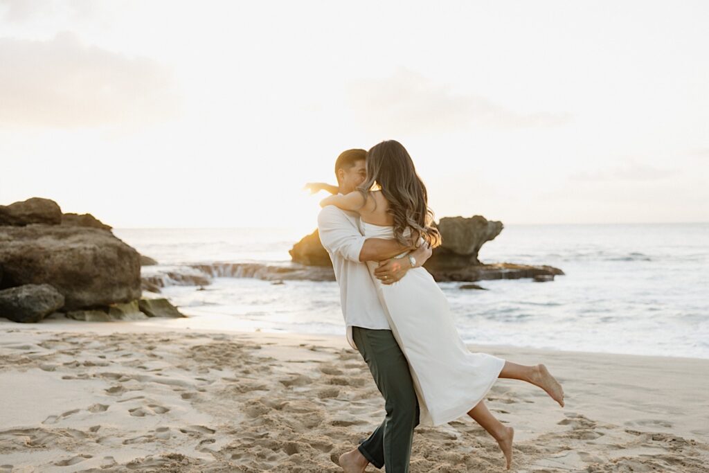 Groom swings his wife around romantically on a beautiful resort vacation beach in Hawaii. 