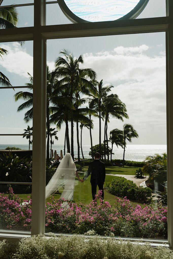 Hawaii Wedding Photographer captures bride and groom outside Chapel window walking together towards the ocean before intimate wedding ceremony at Four Seasons Oahu in Hawaii. 