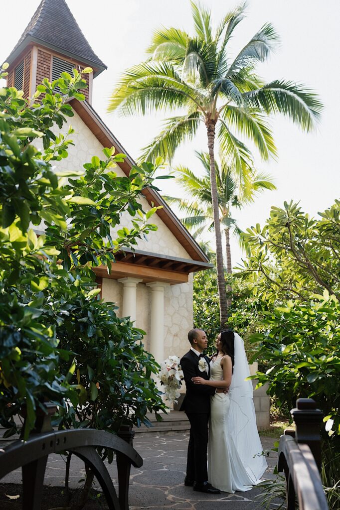 Bride and Groom hold each other outside chapel surrounded by tropical  plants at the Four Seasons Oahu in Hawaii. 