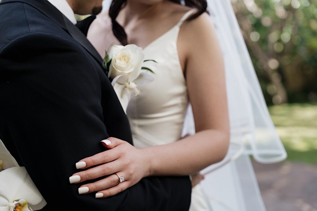 Hawaii Wedding Photographer captures the bride and groom in embrace from the neck down focusing on the bride's beautiful diamond engagement ring. The couple is pictured before their intimate wedding ceremony at Four Seasons Oahu in Hawaii. 