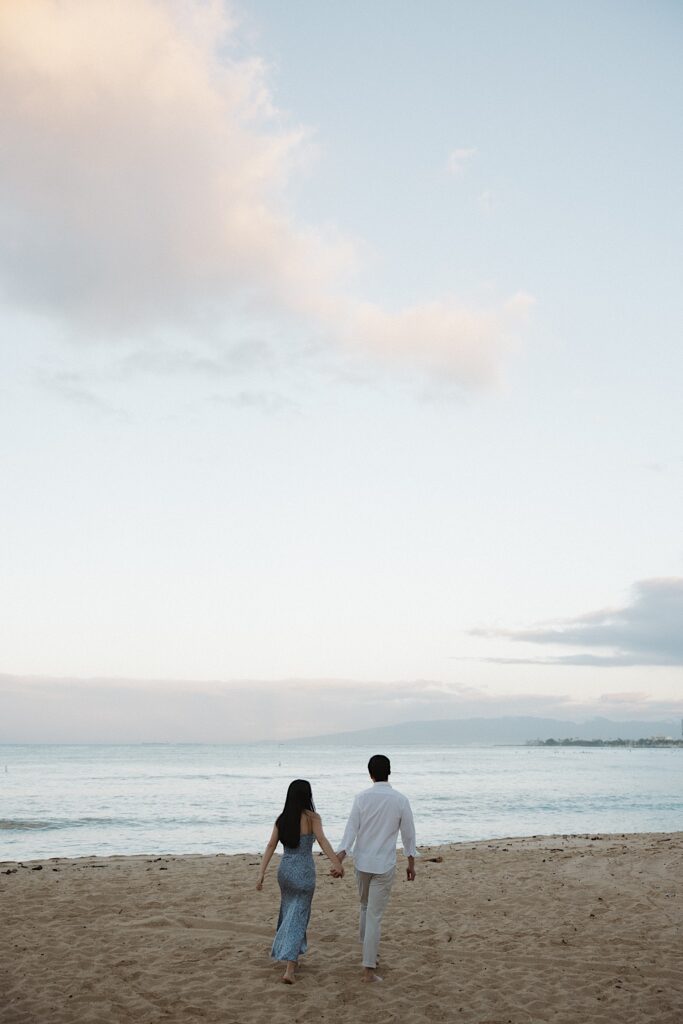 Couple walks away on a beach with the ocean in the background at a beautiful vacation resort for couples in Hawaii. 