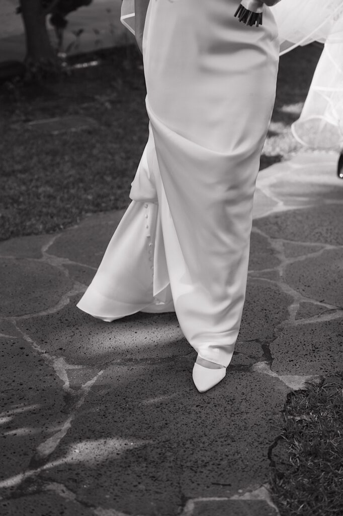 Black and White photo of bride's lower half showing her white shoes popping out from underneath her dress outside Four Seasons Oahu Chapel in Hawaii. 