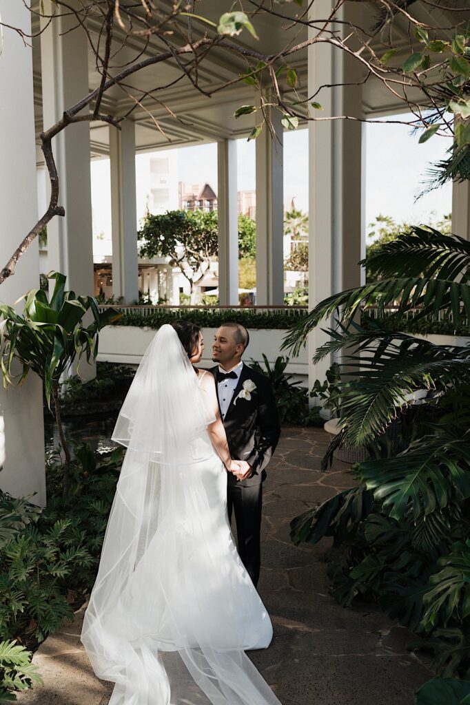 Bride and Groom look at each other standing amongst tropical foliage and plants while holding hands at Four Seasons Oahu in Hawaii. 