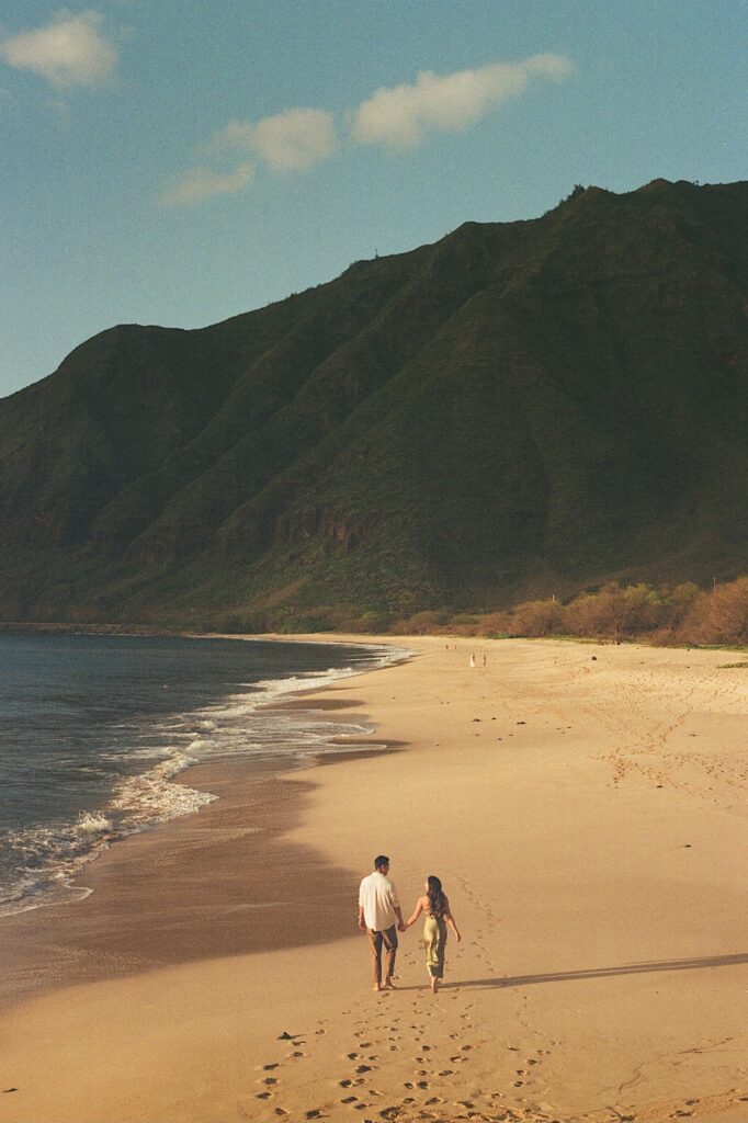 Couple walks in the sand with the ocean and mountains in the background at a gorgeous resort in Hawaii for couples. 