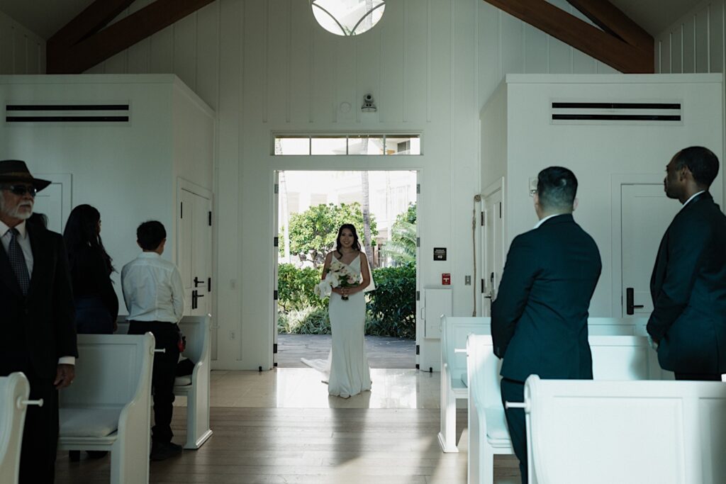 Bride in white gown smiles as she enters the chapel at the Four Seasons Oahu in Hawaii. 