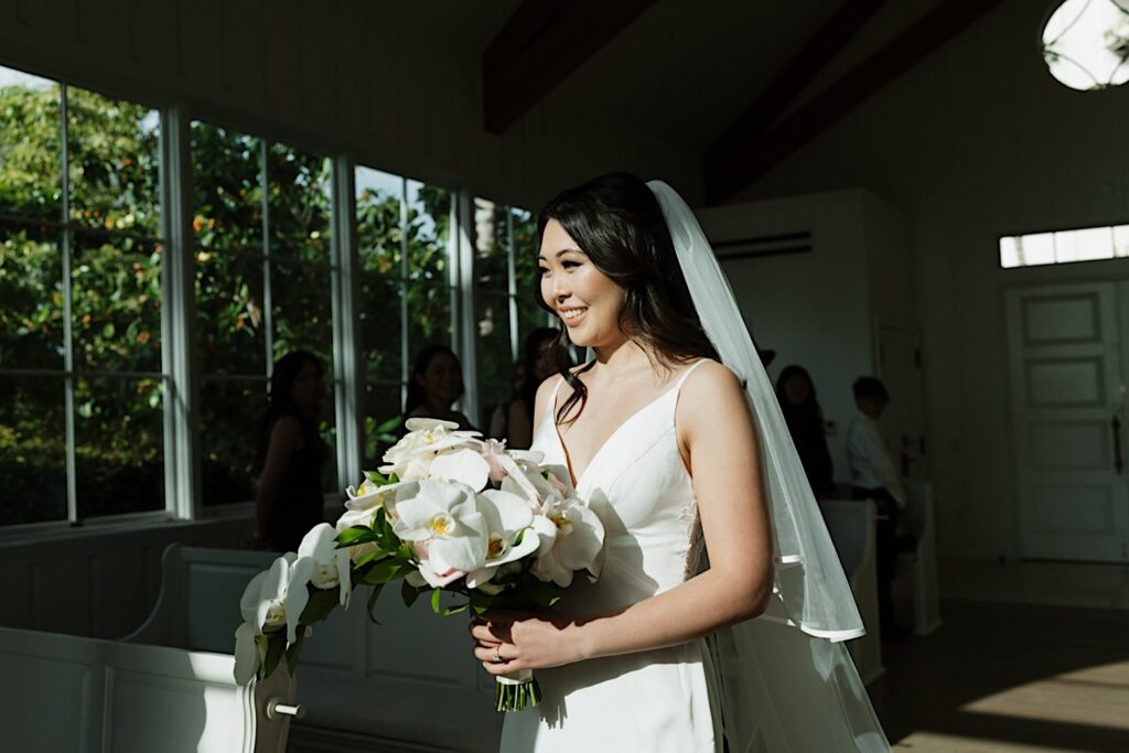 Bride in white gown smiles as she walks down the aisle in intimate wedding ceremony at the Four Seasons Oahu chapel in Hawaii. 