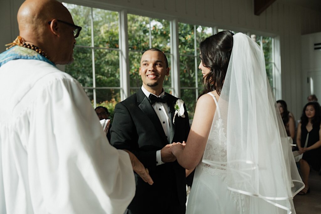 Bride and Groom smile at officiant during intimate wedding ceremony in Four Seasons Oahu Chapel in Hawaii. 