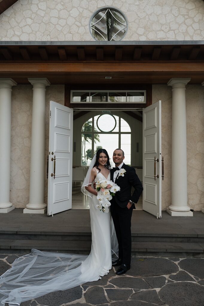 Bride and groom pose smiling outside intimate chapel after intimate wedding ceremony at Four Seasons Oahu in Hawaii.