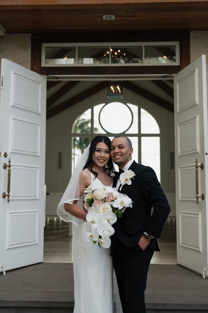 Bride and groom pose smiling outside intimate chapel after intimate wedding ceremony at Four Seasons Oahu in Hawaii.