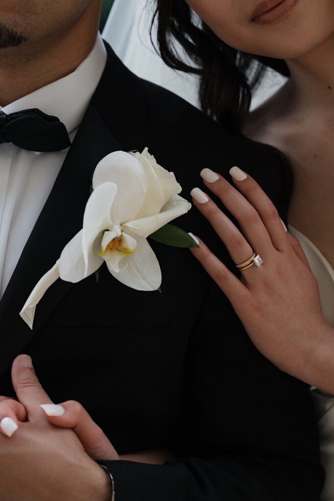 Bride puts her hand on Grooms shoulder next to his tropical boutonniere showing off her beautiful diamond engagement ring at Four Seasons Oahu in Hawaii. 