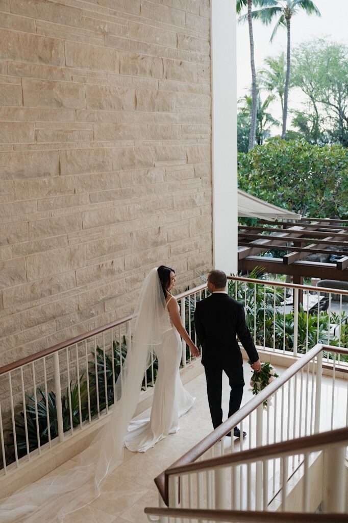 Bride with long flowing white veil and Groom Walk down the steps overlooking beautiful tropical scenery at the Four Seasons Oahu in Hawaii.