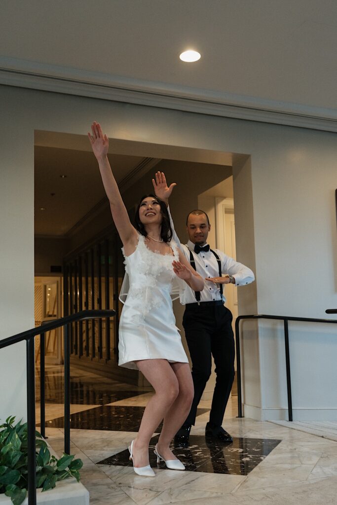 Bride in short white dress dances with Groom entering wedding reception at Four Seasons Oahu in Hawaii. 